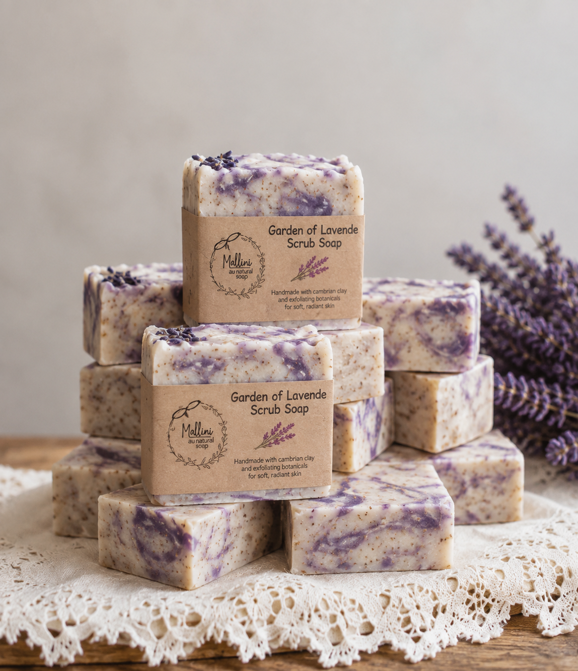 A stack of handmade lavender scrub soap bars wrapped in kraft paper labels, displayed on a lace doily with dried lavender sprigs in the background.